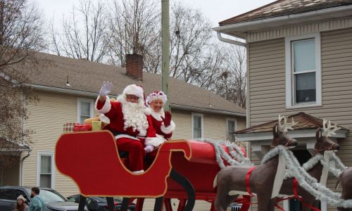 Santa and Mrs. Claus waving from a sleigh during a small-town Christmas parade