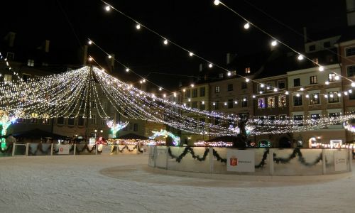 Strings of holiday lights over an outdoor plaza with a Christmas tree