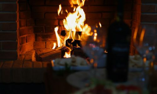 Glass of red wine and a bottle beside a crackling fireplace