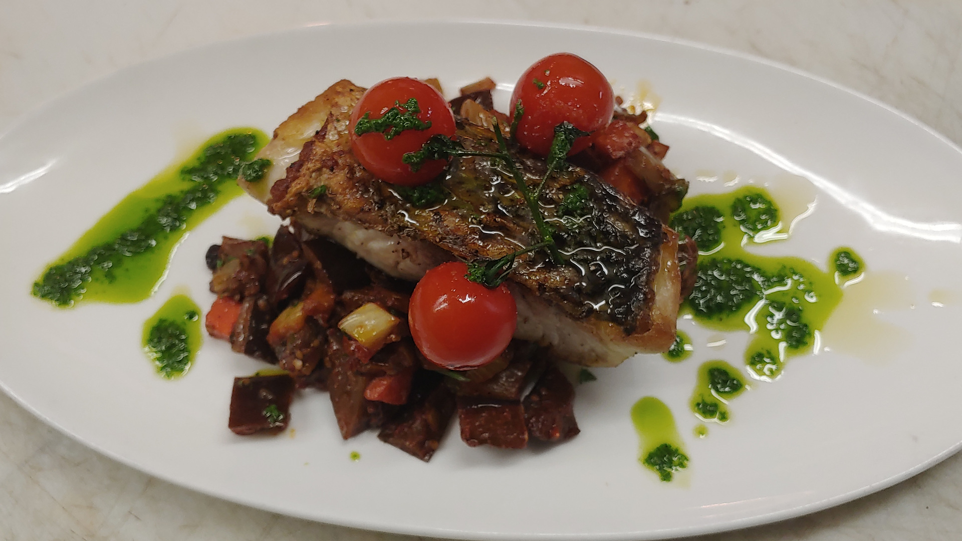 Seared fish with cherry tomatoes and herb oil, plated at Nick & Toni's in East Hampton
