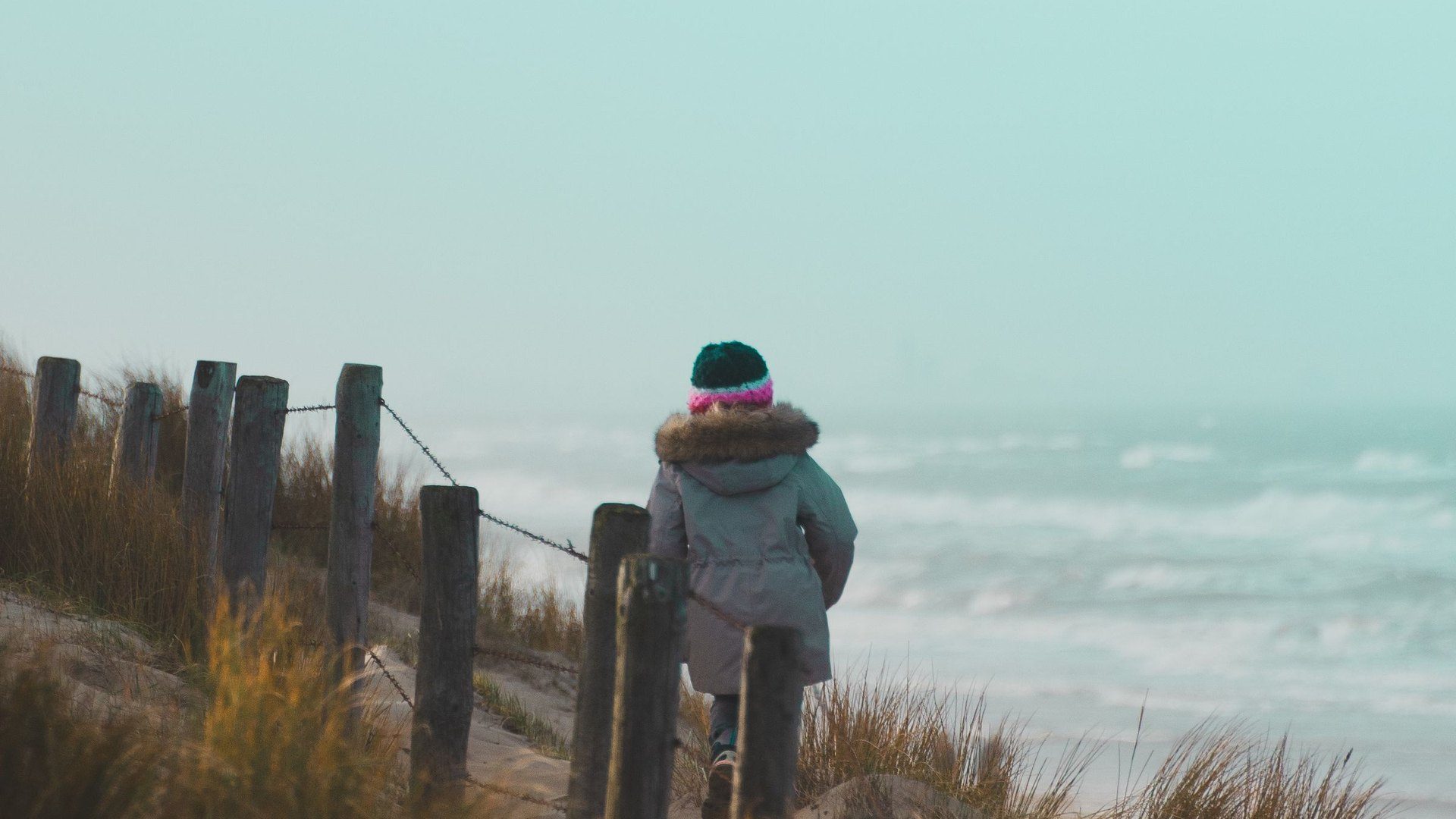 Child in a winter hat walking along a beach path between sand dunes